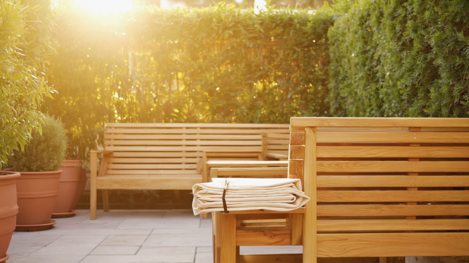 Verwitterte Teak-Gartenmöbel auf einer Terrasse mit Topfpflanzen und zusammengelegtem Sonnenschirm im Nachmittagslicht
